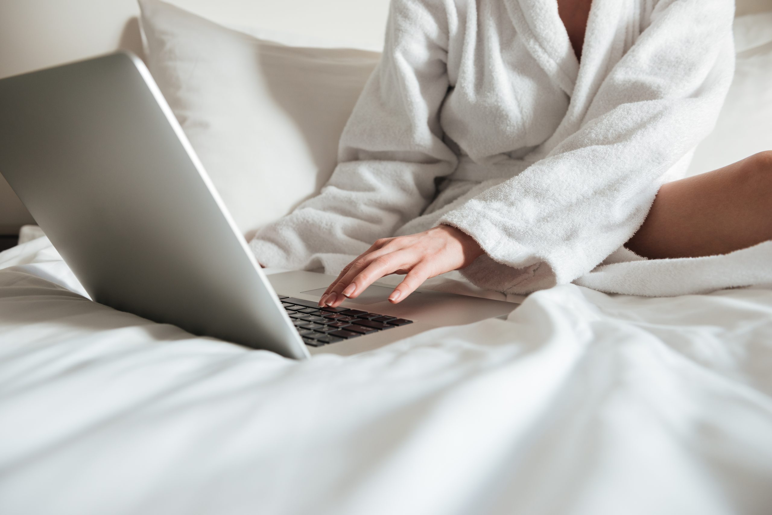 Cropped image of a woman in bathrobe on bed and using laptop Cropped image of a woman in bathrobe on bed and using laptop in a hotel room
